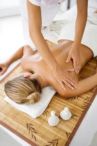 Profissional fazendo massagem nas costas de uma pessoa deitada em um ambiente claro e tranquilo